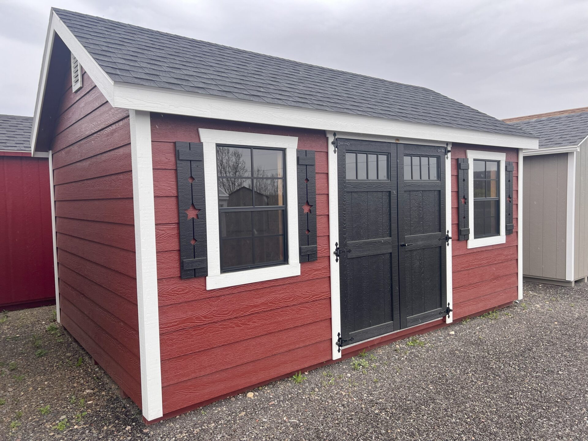 Red lap sided shed with double black doors with transom windows and two windows with shutters