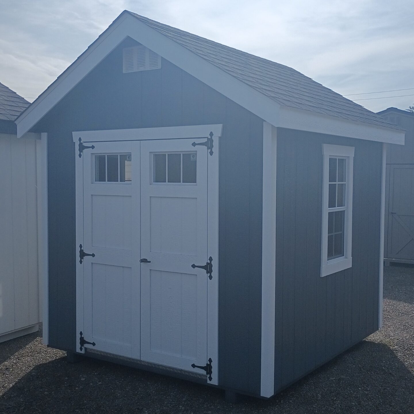 Small shed with peaked roof, double doors with transom windows and two large windows on either side