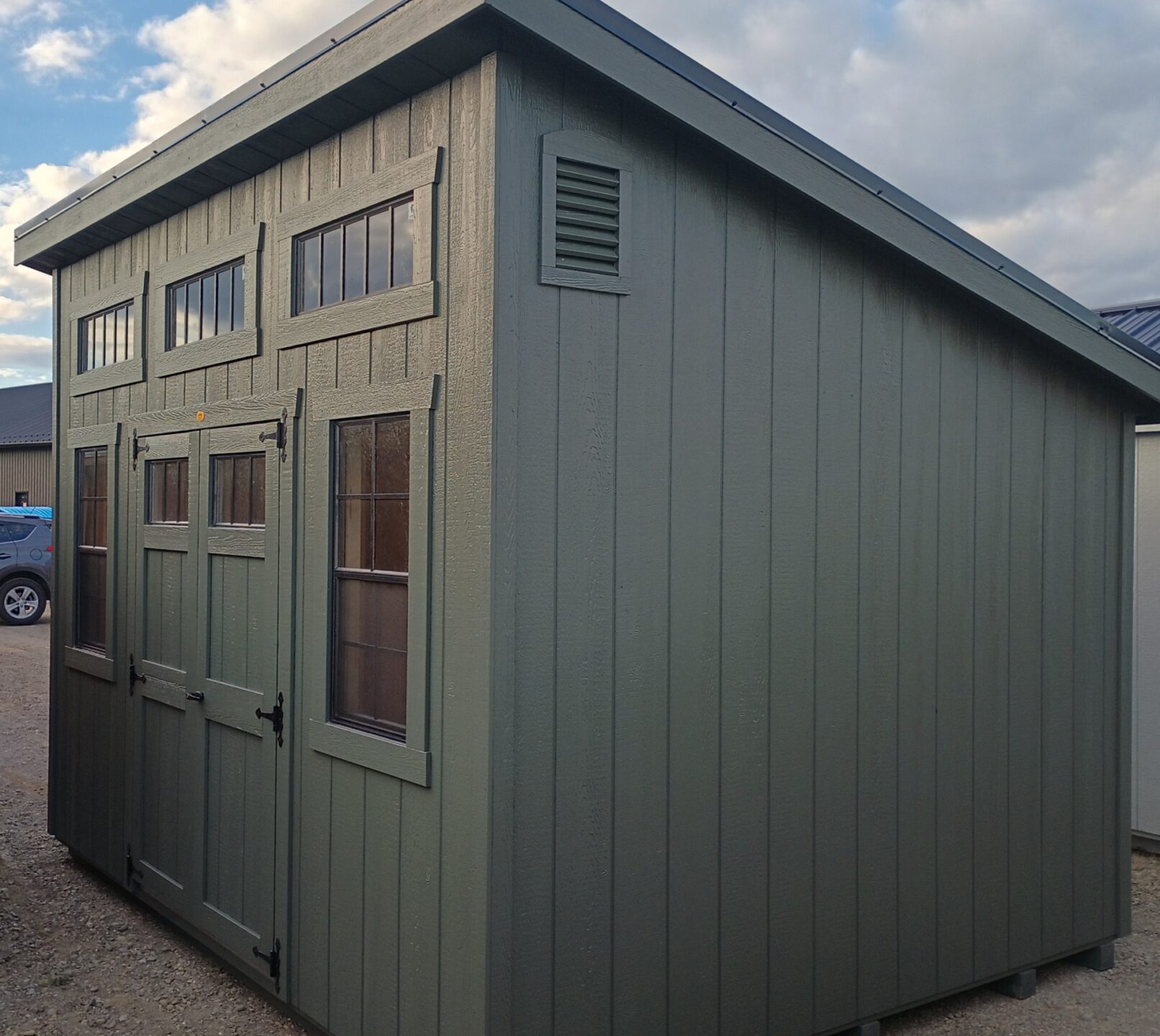 One slant green shed with double doors, two windows and transom windows above