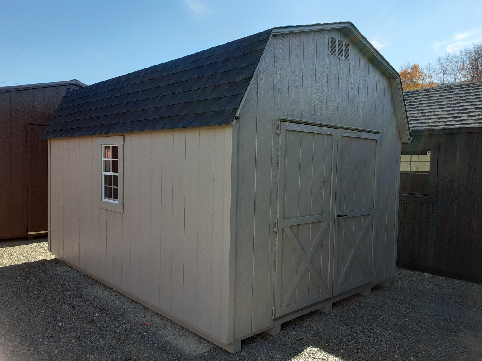 Small clay colored shed with double doors, shingles and windows on either side