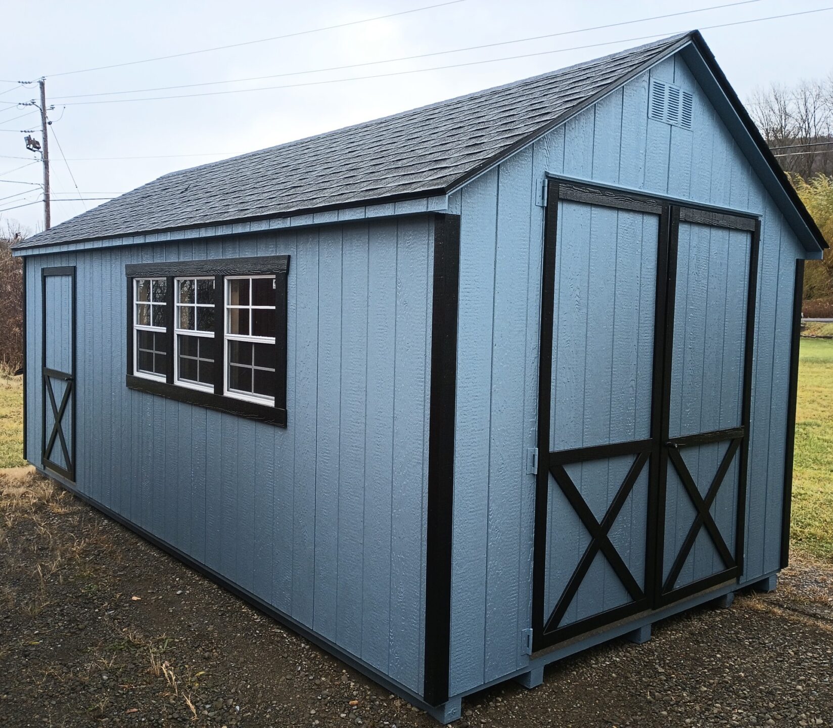 Large blue shed with black trim, double doors, single doors, shingled roof and three windows