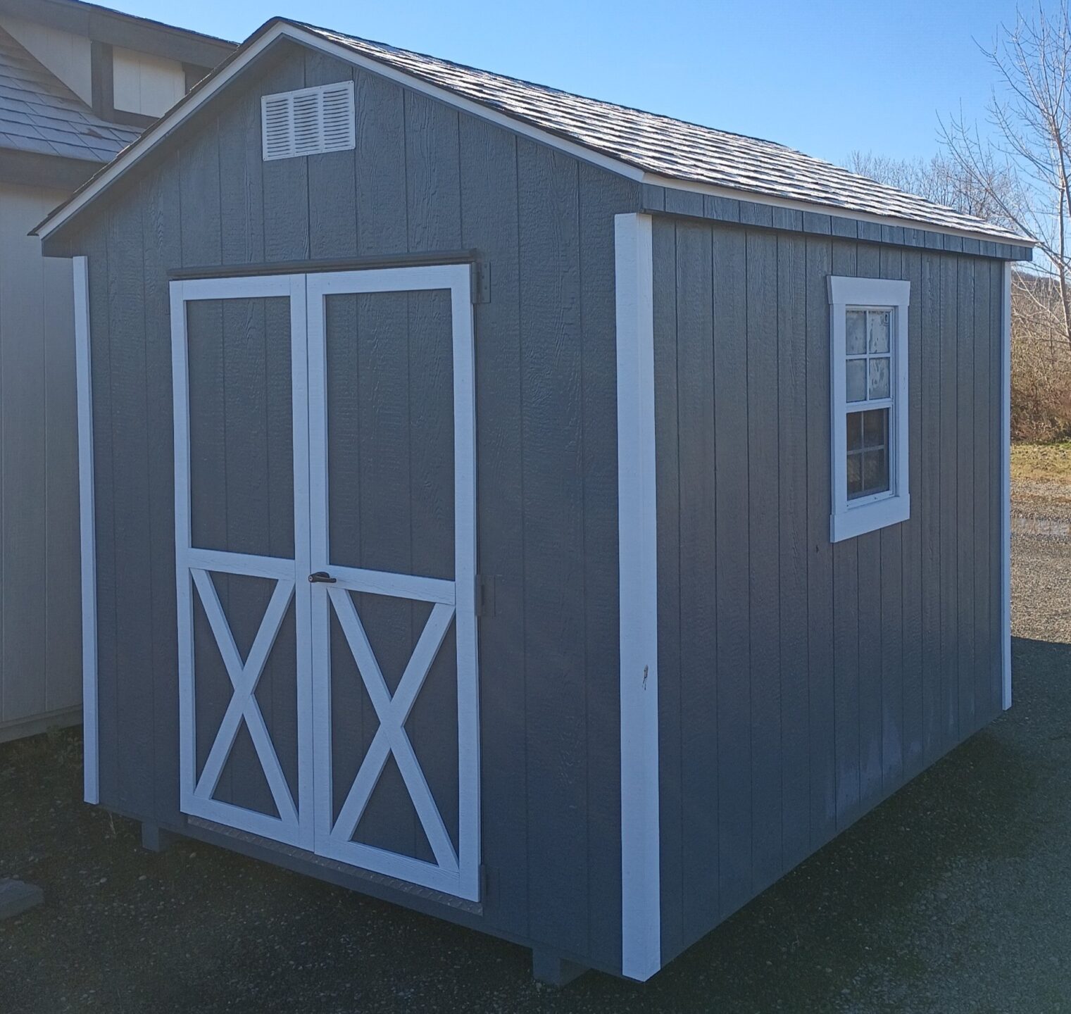 Small dark gray shed with white trim and double doors with two windows and shingled roof