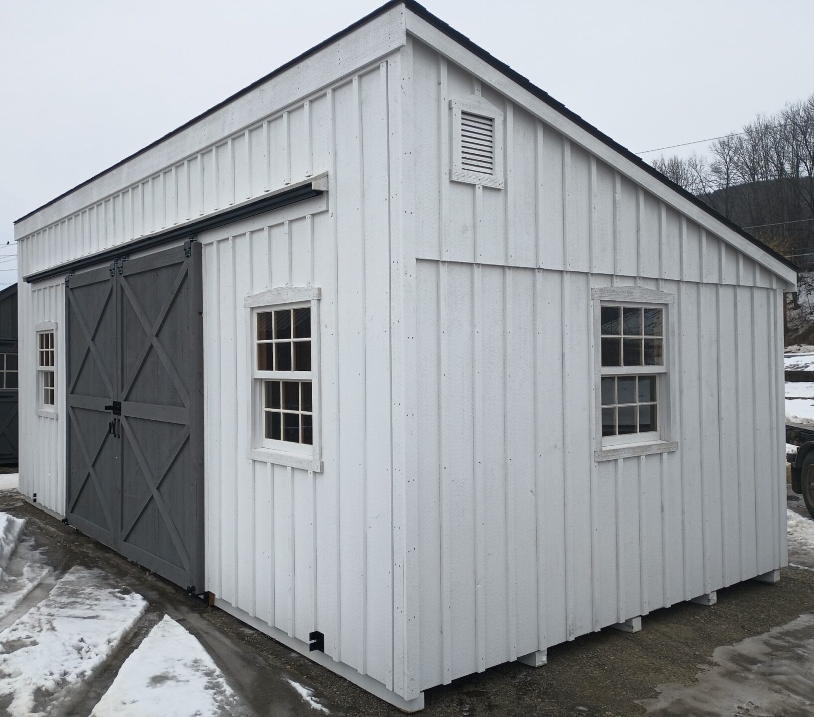 Large white board and batten shed with gray sliding barn doors and 4 wooden windows