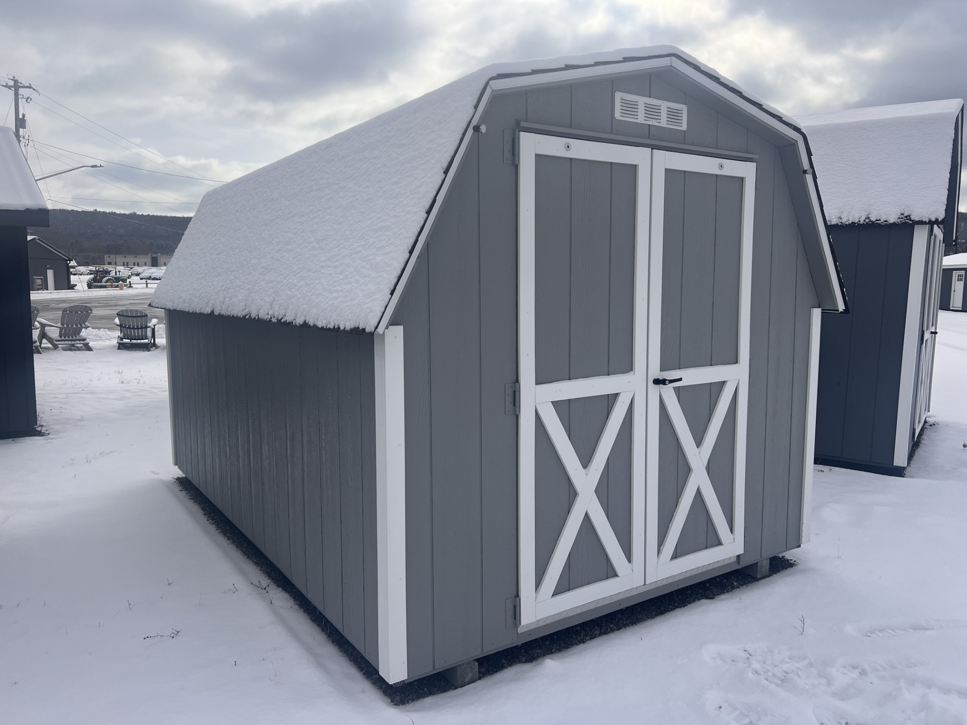 Small barn style gray shed with white trim and double doors at end and one window at other end