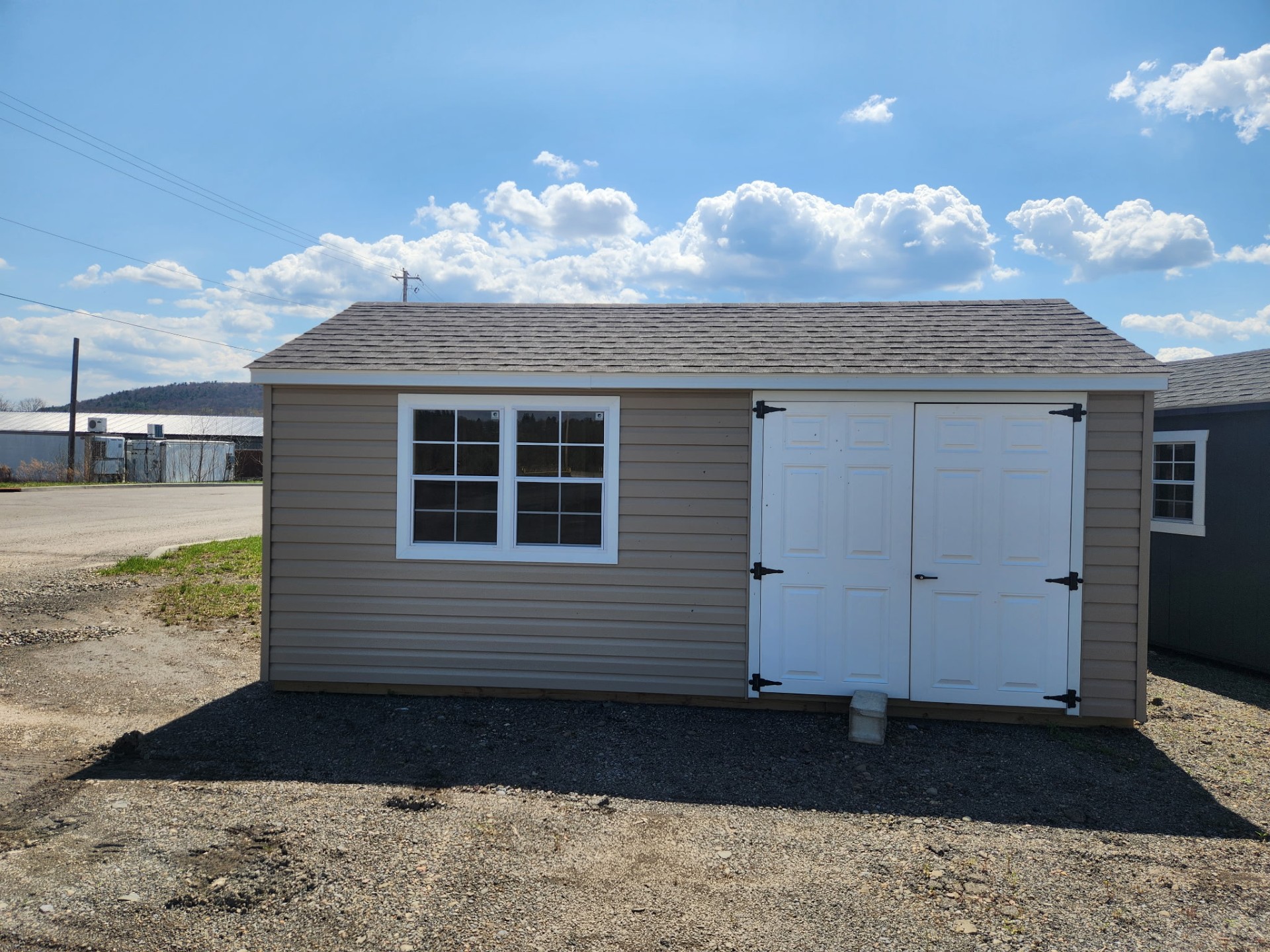 Tan color vinyl shed with white double doors and two windows on long end