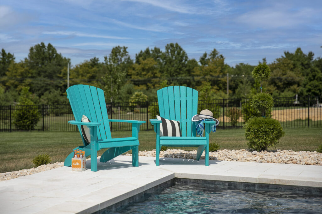 Two turquoise Adirondack Chairs set along the edge of an inground pool on a beautiful summer day