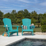 Two turquoise Adirondack Chairs set along the edge of an inground pool on a beautiful summer day