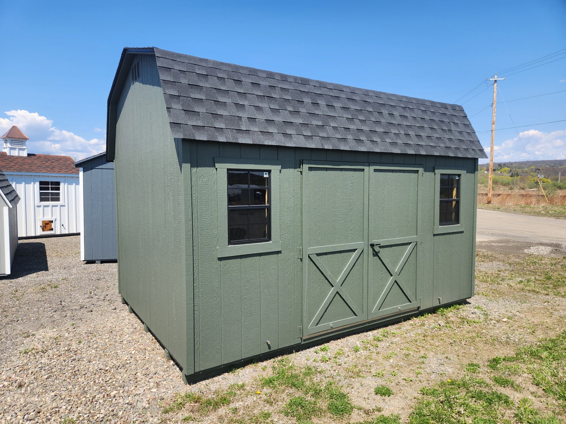 Green shed with barn roof, double doors, two windows and shingled roof