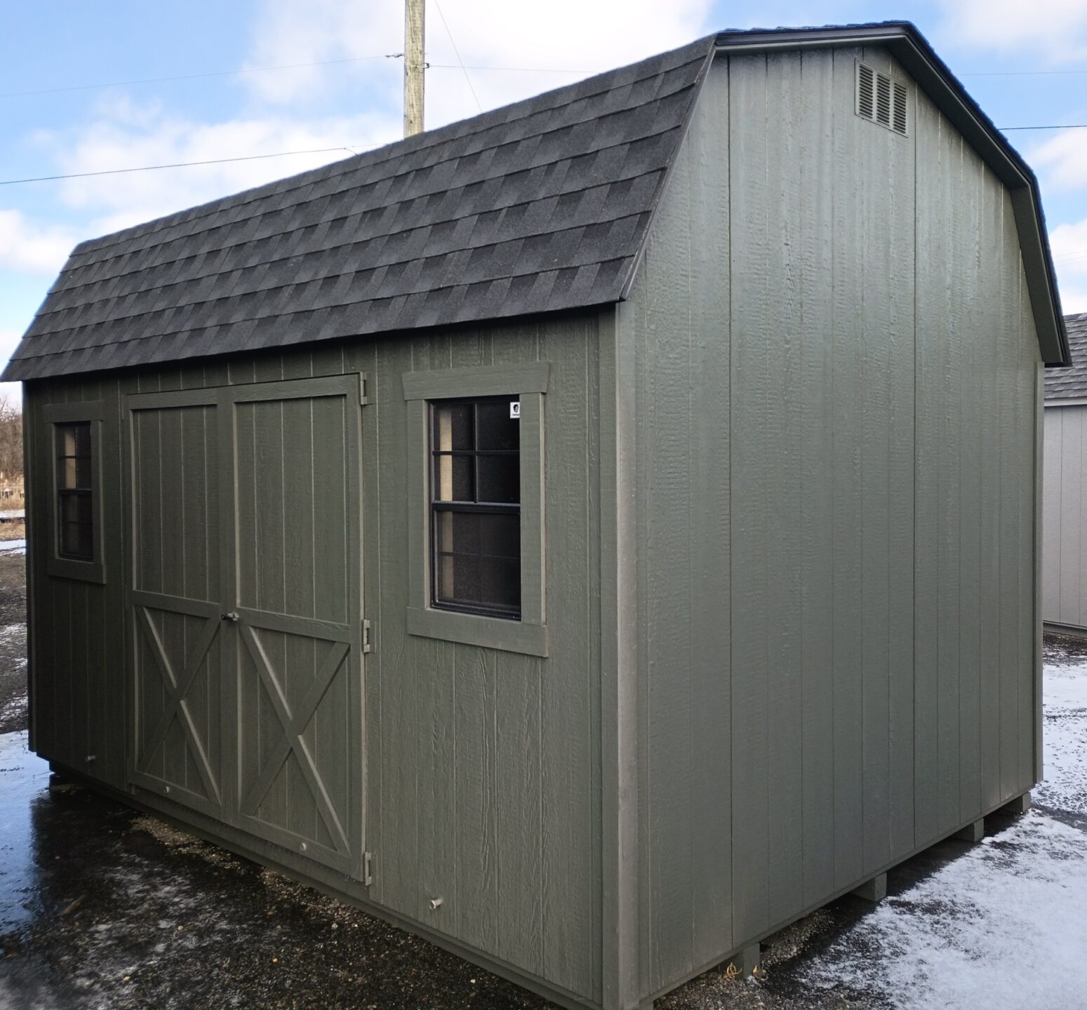 Green shed with barn roof, double doors, two windows and shingled roof