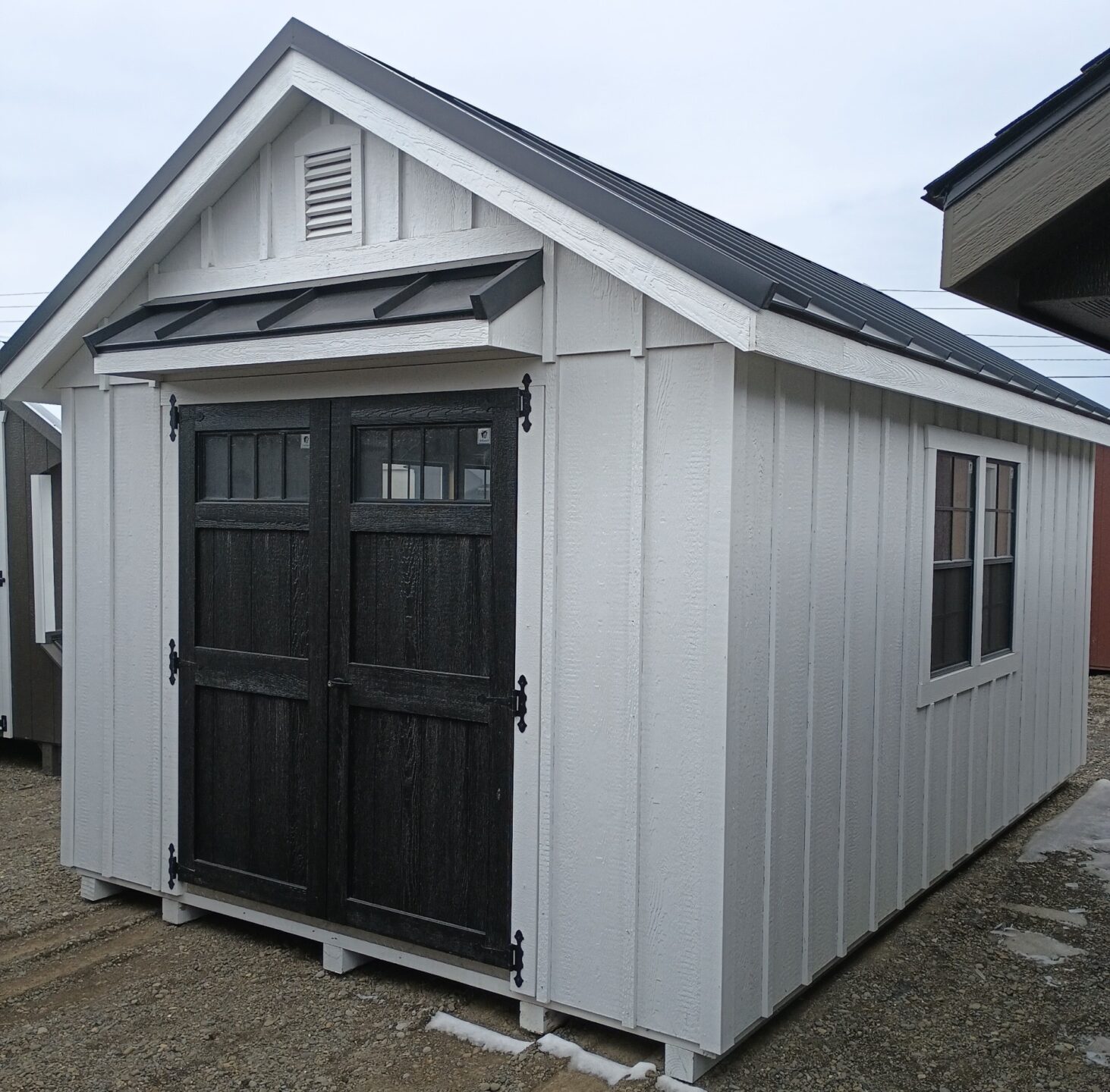 Small white shed with black doors and pent roof over, gable vents and windows on either side