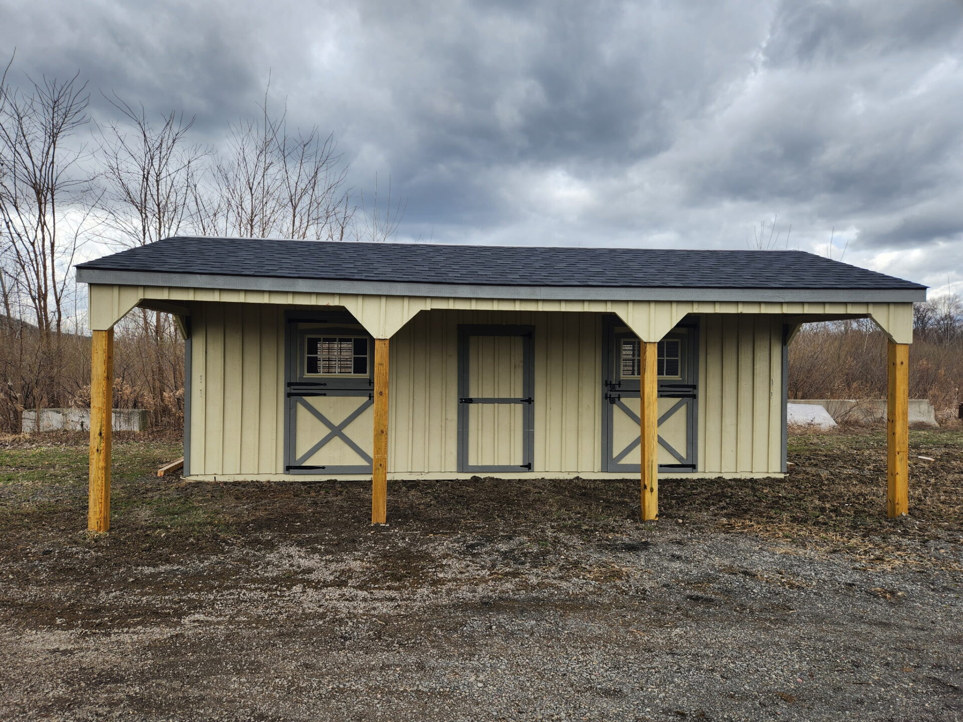 Horse barn with overhang, tack room in center and a stall on either side.