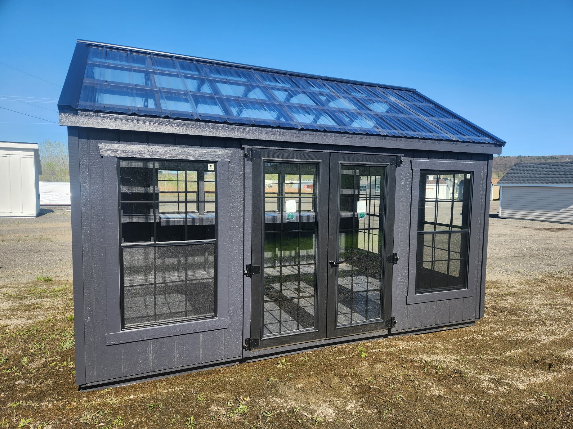 Black greenhouse with glass doors and windows all around with clear roofing panels
