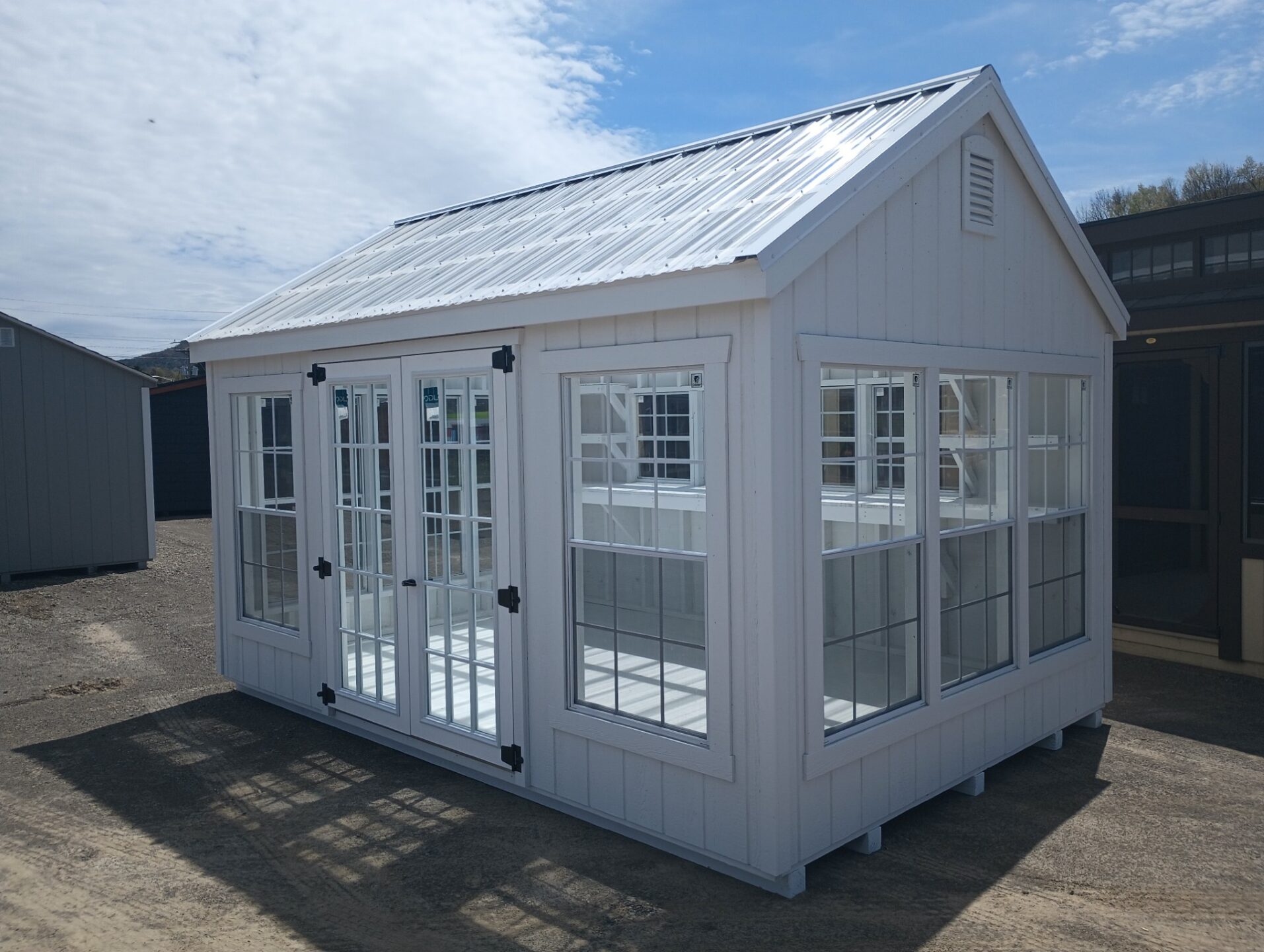 White greenhouse with windows all around and glass double doors with grids. Clear roof panels
