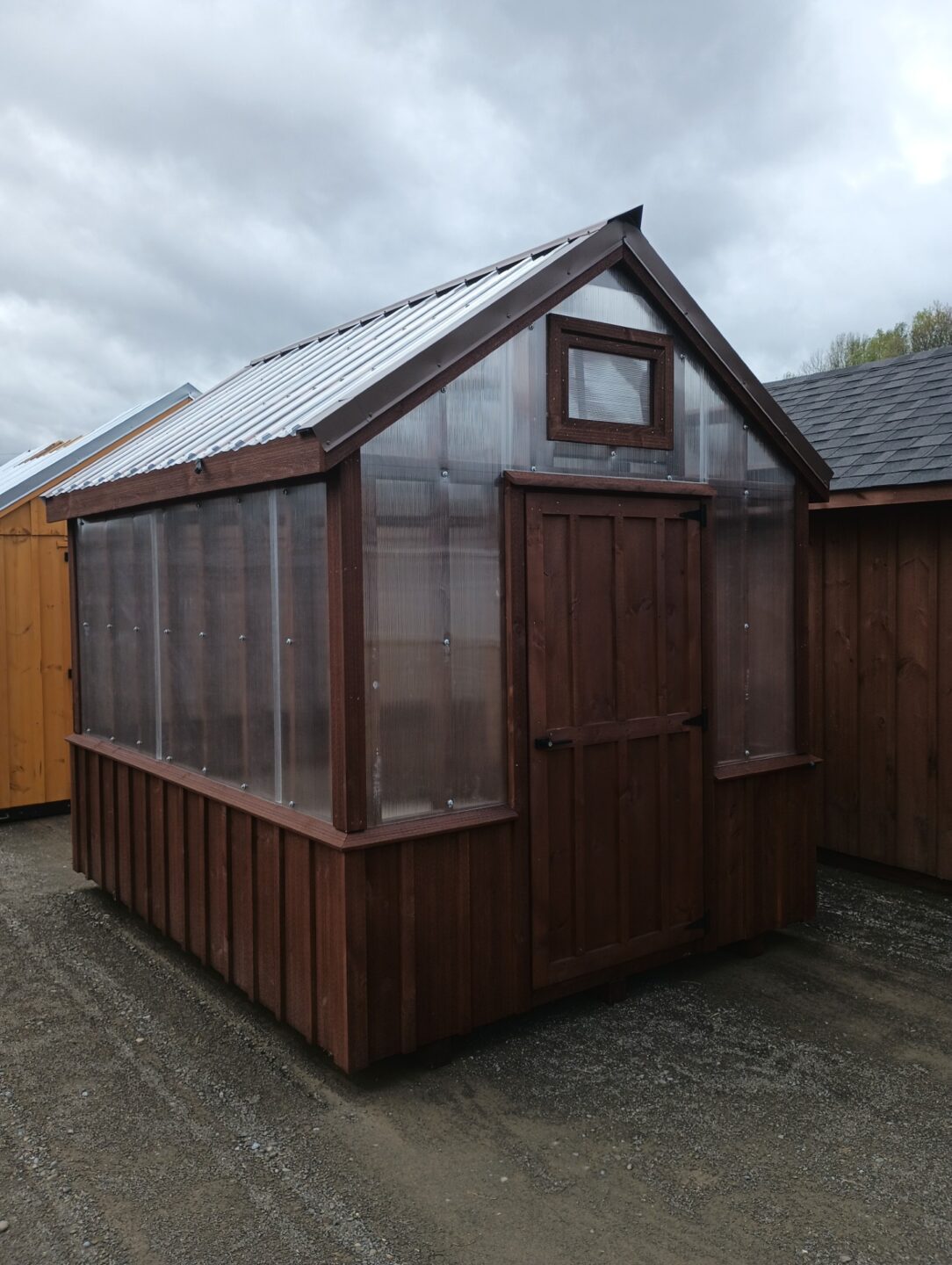 Small peaked roof greenhouse with board and batten knee wall and clear roof panels