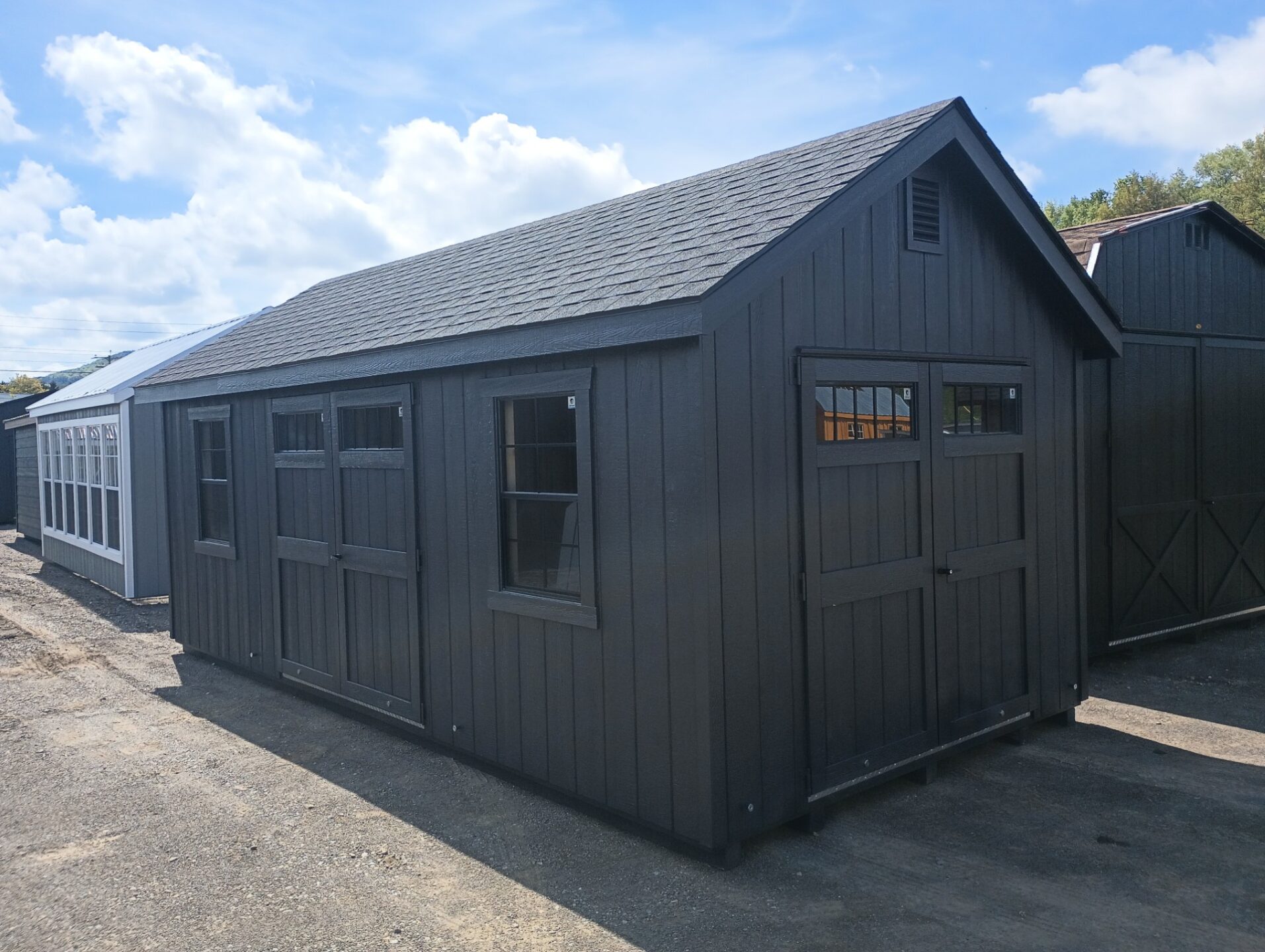 Dark color shed with double doors at the end and double doors on long wall with two windows on each side
