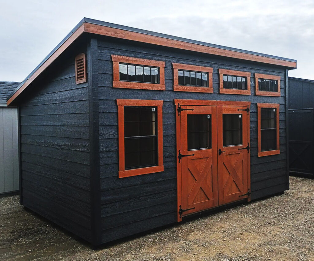 A shed building by with dark wood siding and brown doors and trim. Contact Amish Barn Co to get yours today.