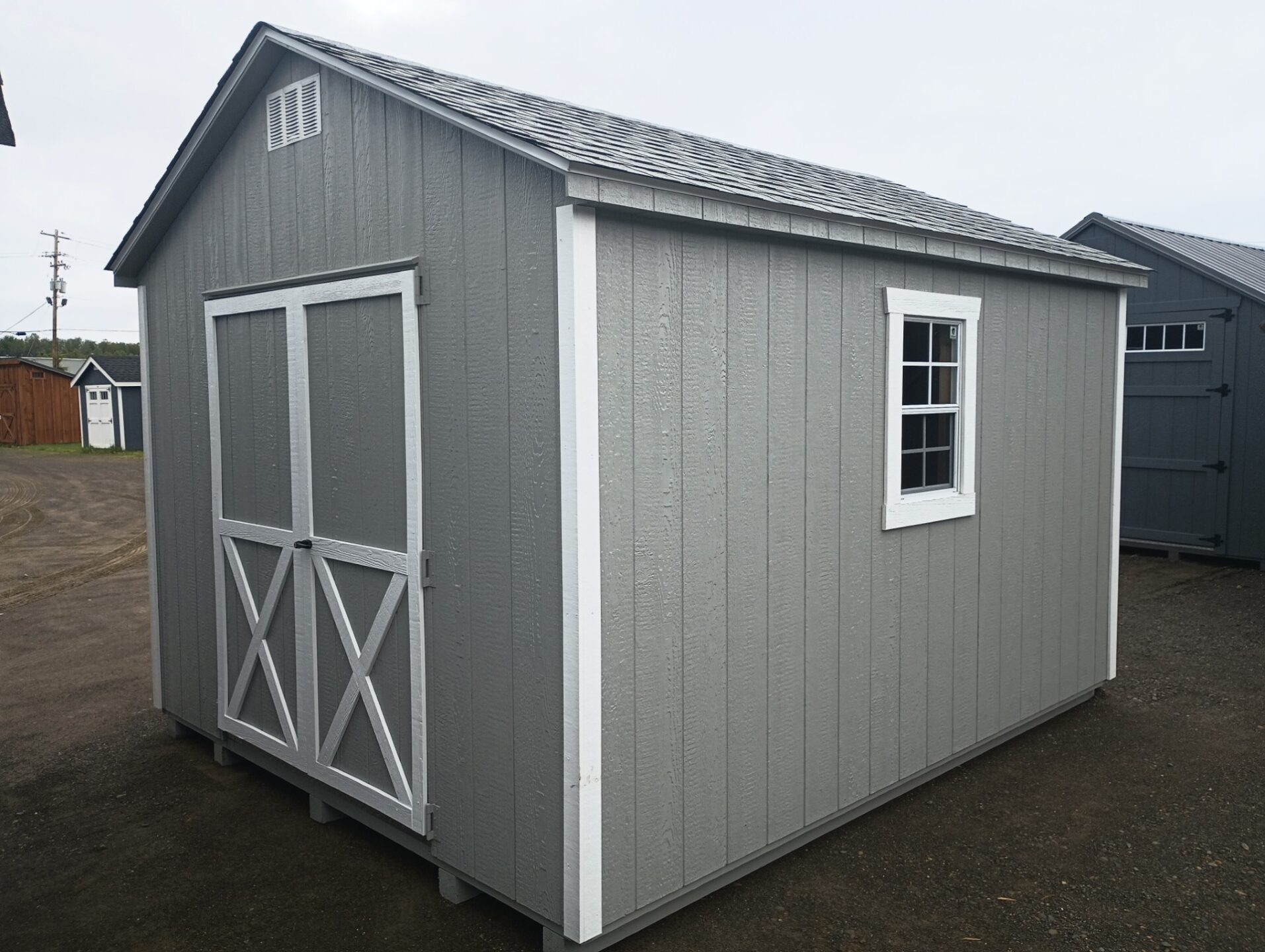 Small grey and white shed with double doors, two windows and shingled roof