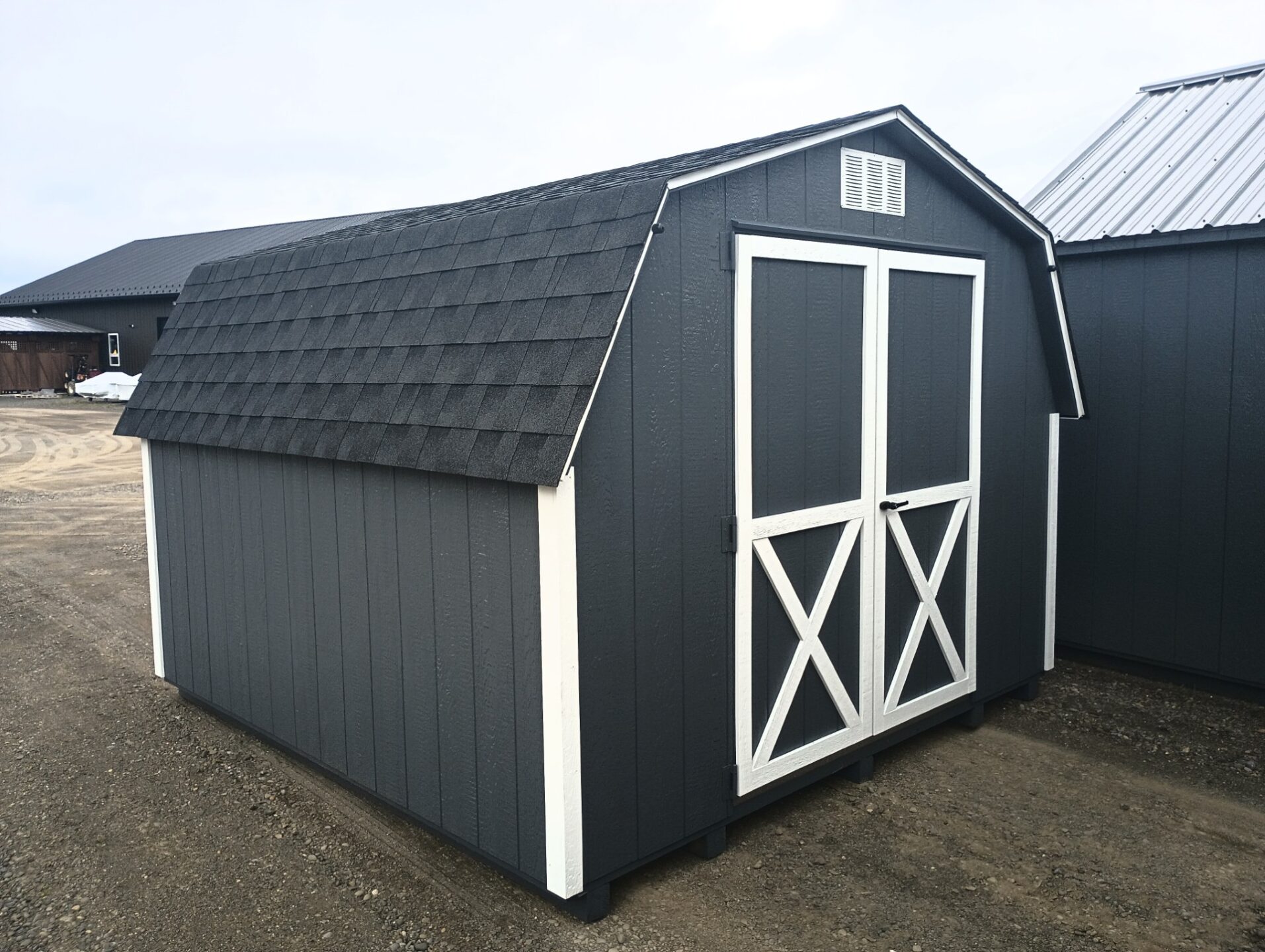 Small dark gray shed with white trim and double doors, shingled roof and window on back wall