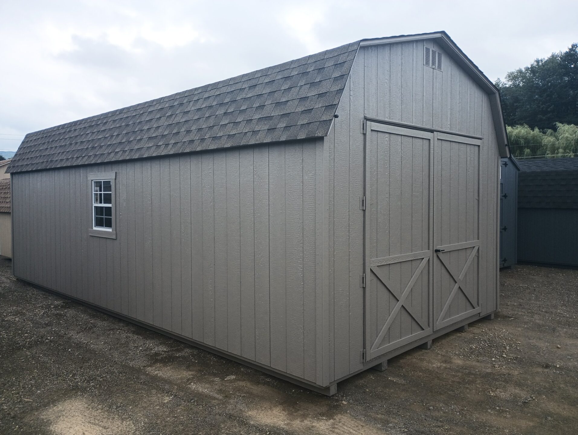 Large clay color barn shed with large double doors, shingled roof and windows on either side