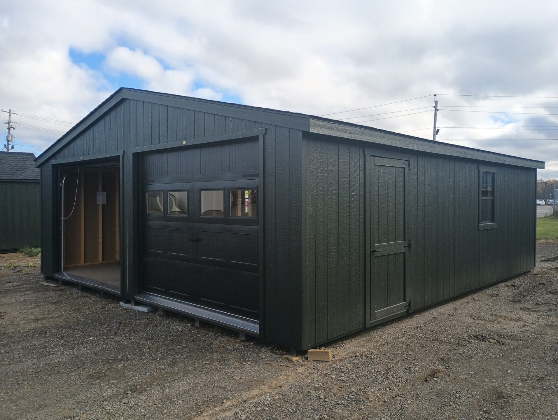 Double garage with a dark green color, black overhead carriage style doors, side door, 3 windows and shingled roof