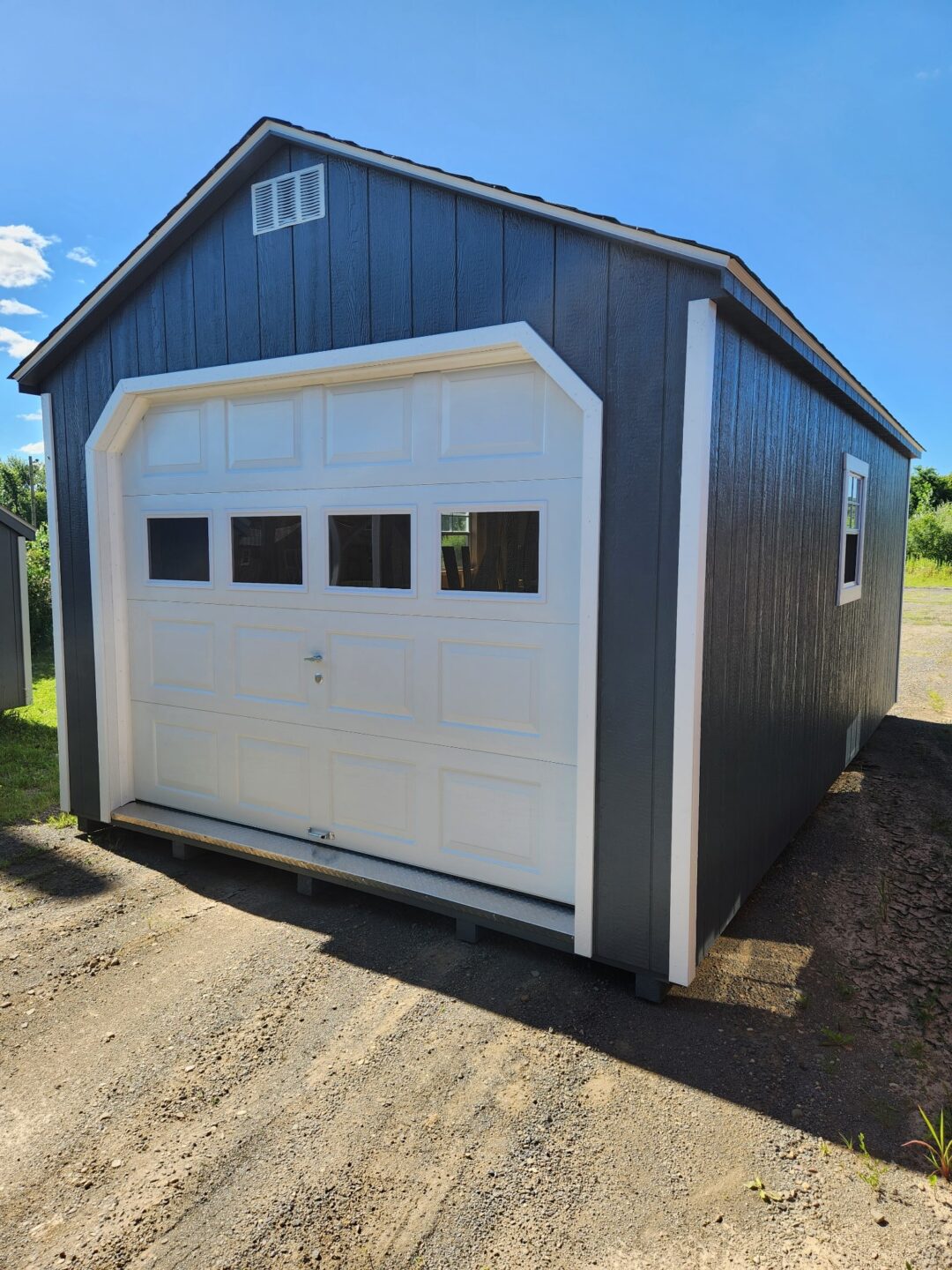 A frame garage with overhead door with glass, shingled roof, two windows and a door on the side