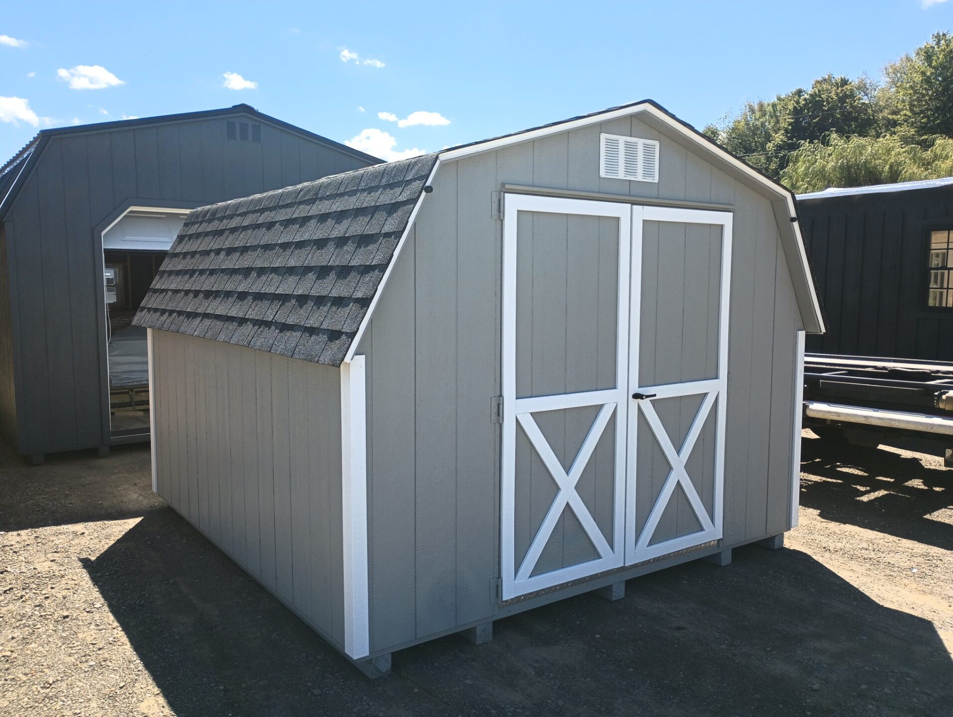 Small grey wall barn with white trim, shingled roof and double doors