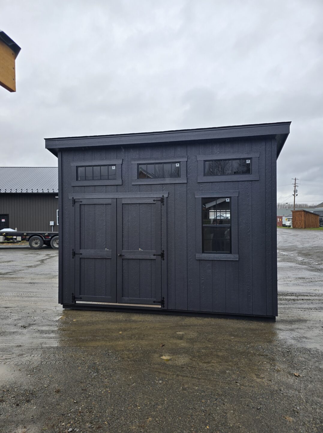 One slant shed with painted siding, shingled roof, double doors and 3 transom windows across the back wall
