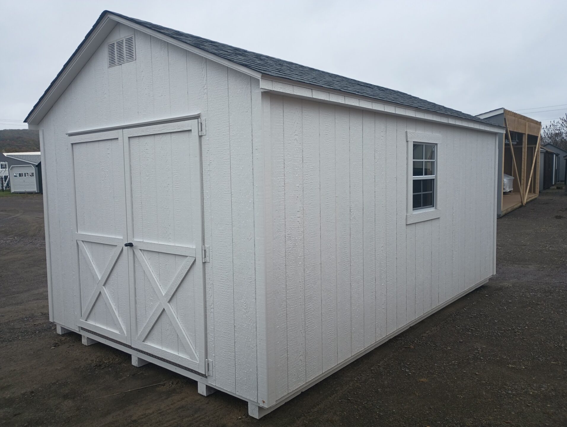 White shed with double doors, vents, windows and shingles on the roof