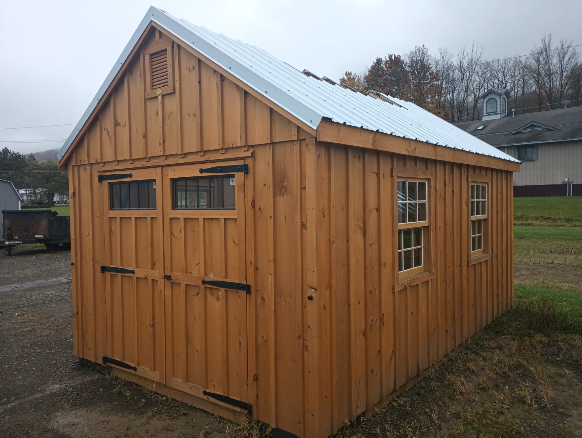 Board and Batten sided shed with double doors with transom windows, metal roof with opening for cupola and 2 windows on either side