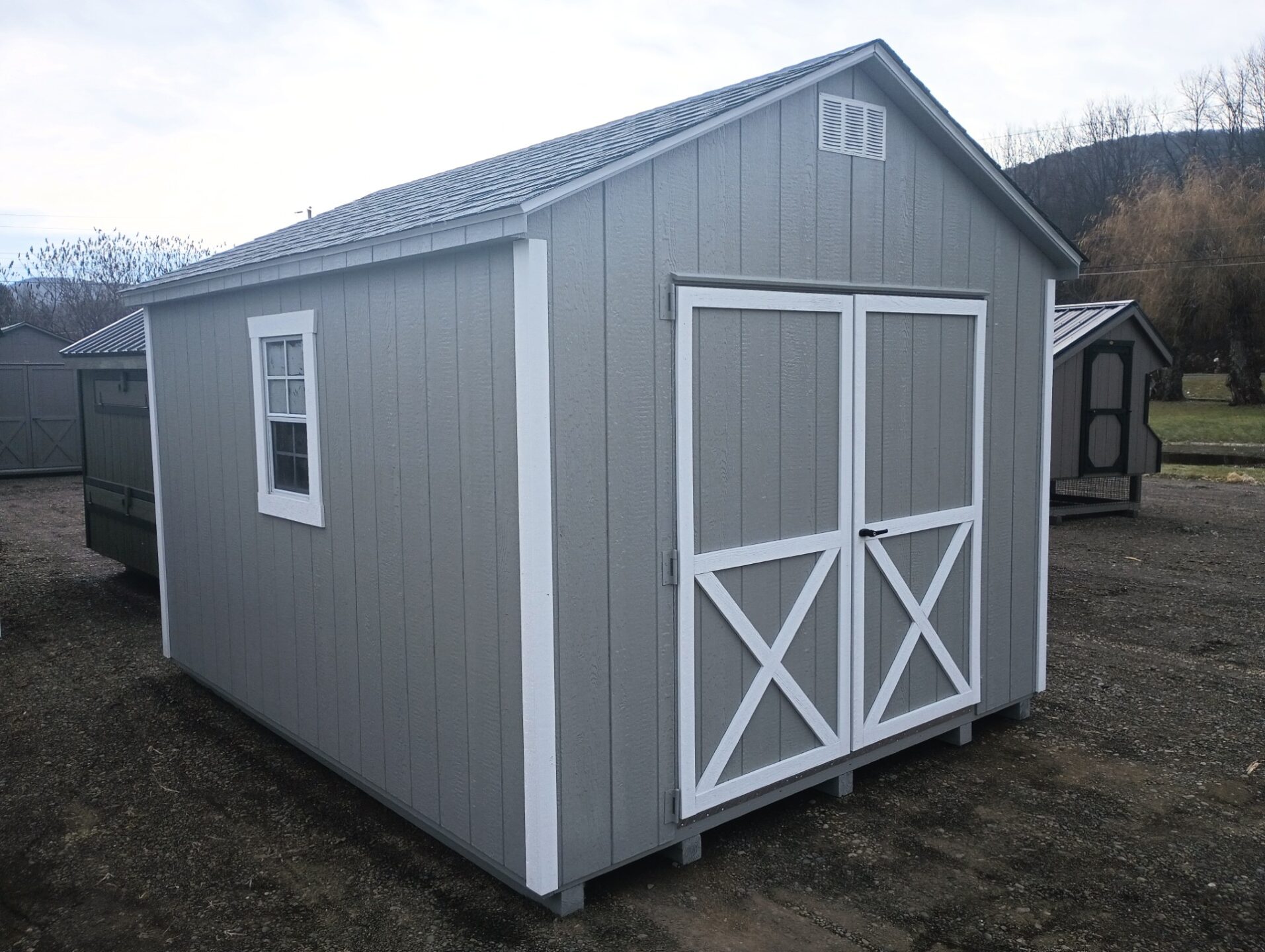 Light gray shed with white trim, double doors, two windows and shingled roof