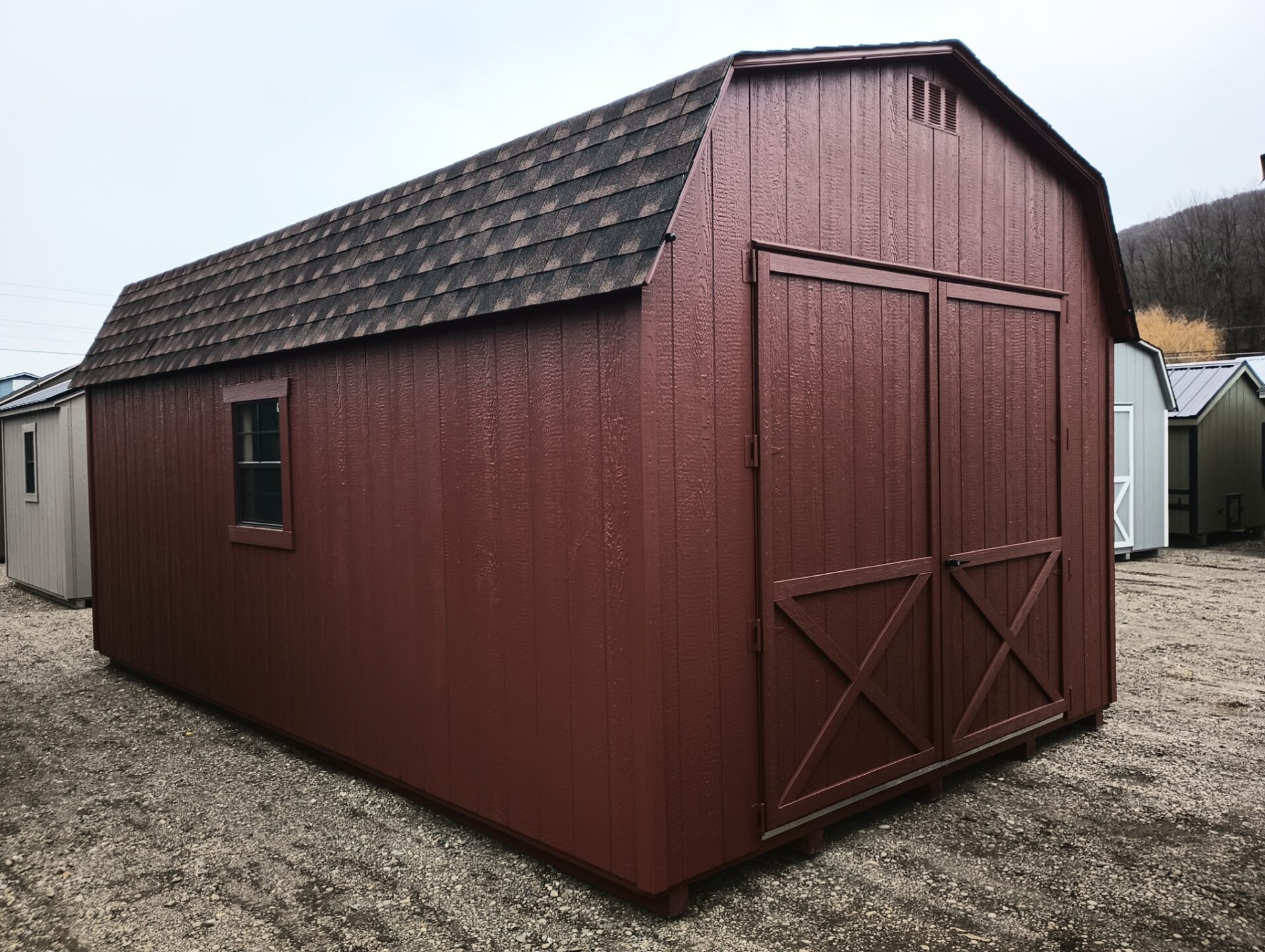 Barn style shed with red siding and trim, shingled roof, large double doors on the end and windows on either side