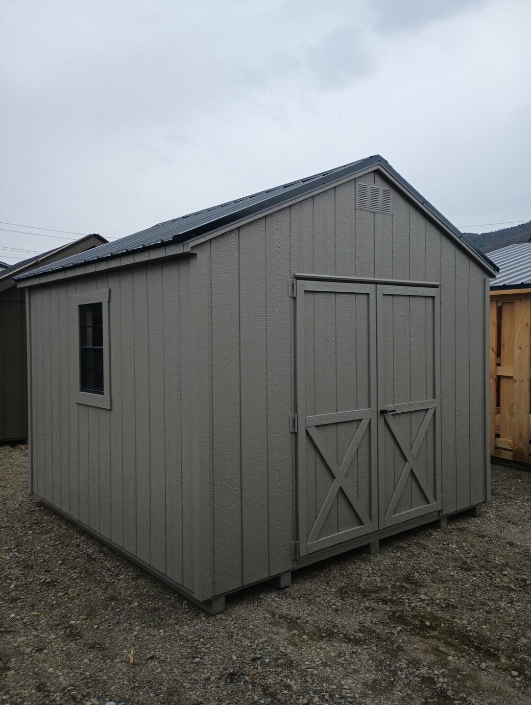 Small clay colored shed with peak roof, double doors, metal roof and windows on either side