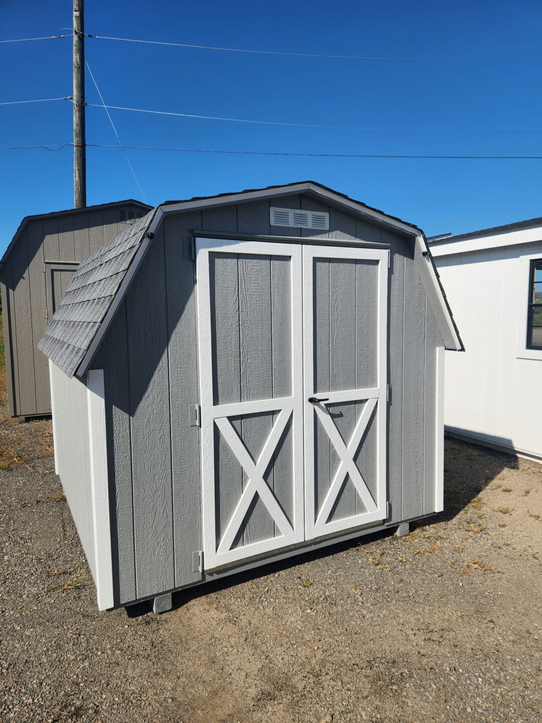 Small gray barn shed with white trim and shingled roof, double doors on the front