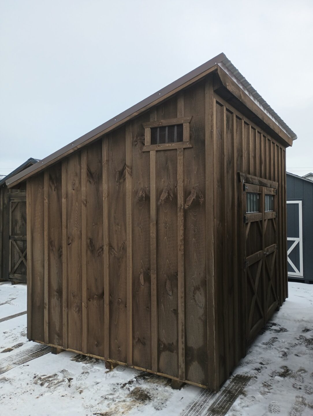 Shed with board and batten siding and one slant roof, stained a mushroom color with brown metal on roof
